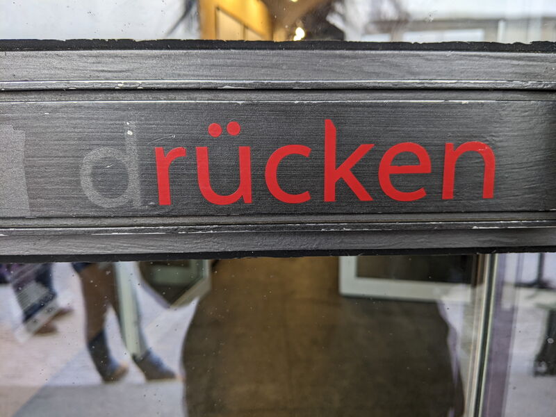 Schild „drücken“ an der Glastür, im Spiegelbild der Flur