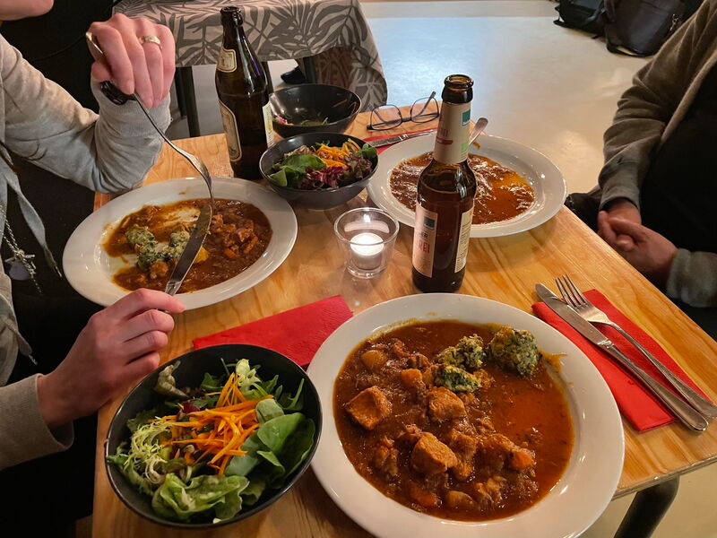 Teller mit Gulasch, Knödel und Salat auf einem Holztisch, daneben eine Flasche Bier